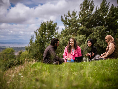 Students on the grass in Ashton park with Morcambe bay in the distance