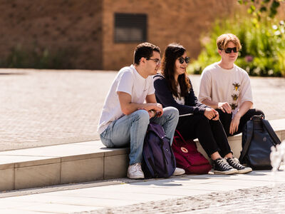 three students sat on step on campus in sunshine
