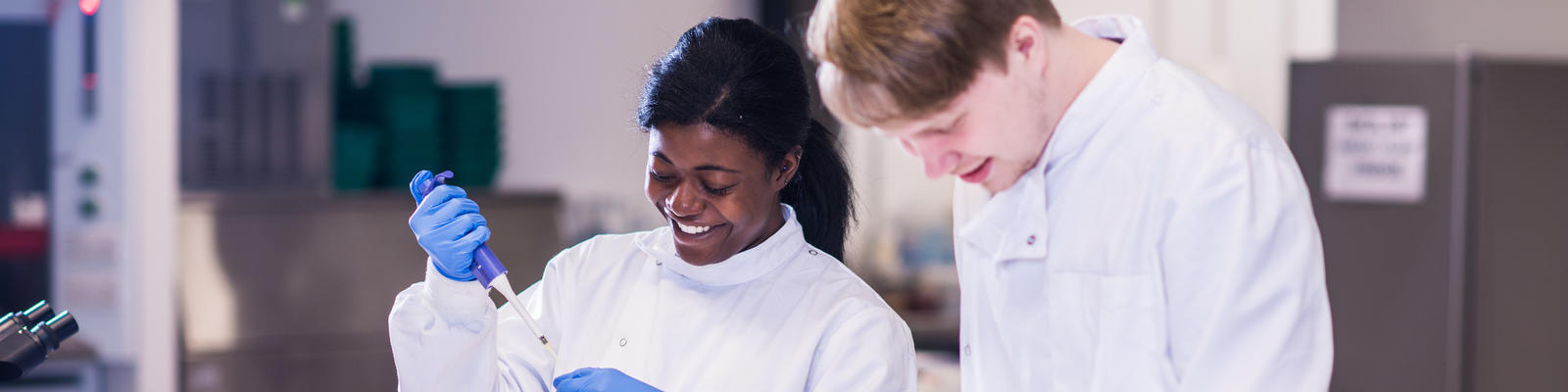 Two students work collaborate on work, with one using a pipette to measure liquid.