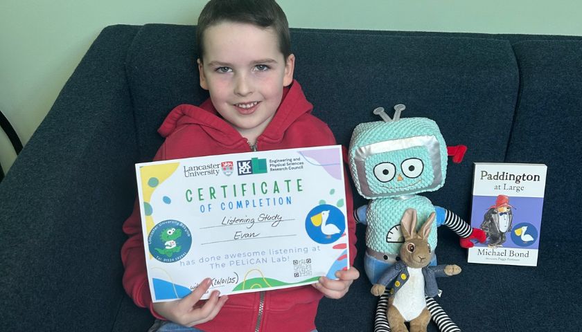 A young boy holding a certificate whilst sat next to Beep Beep the robot
