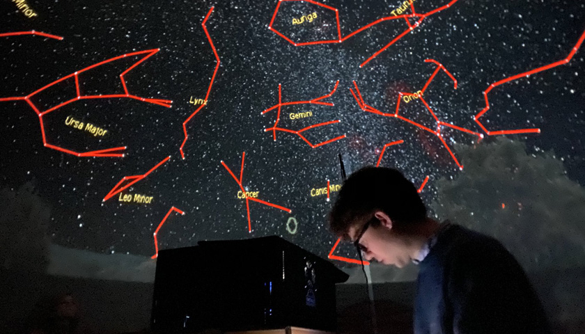 An academic stands in front of a projection of the galaxy with the constellations labelled