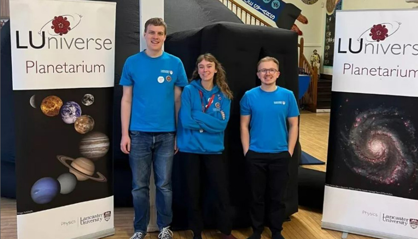 Three students in blue t-shirts stood in front of the Planetarium