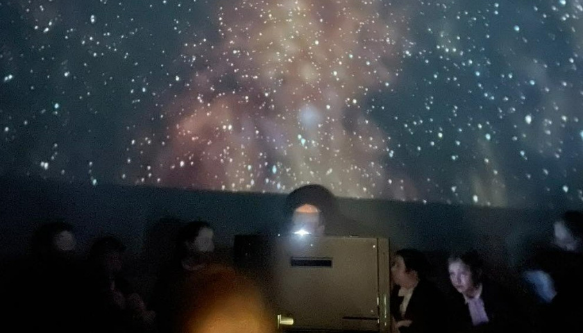 A group of students and their teacher sat in front of a projection of the galaxy
