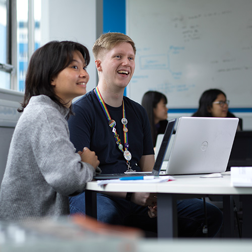 Two students sat at a desk with a laptop in front of them