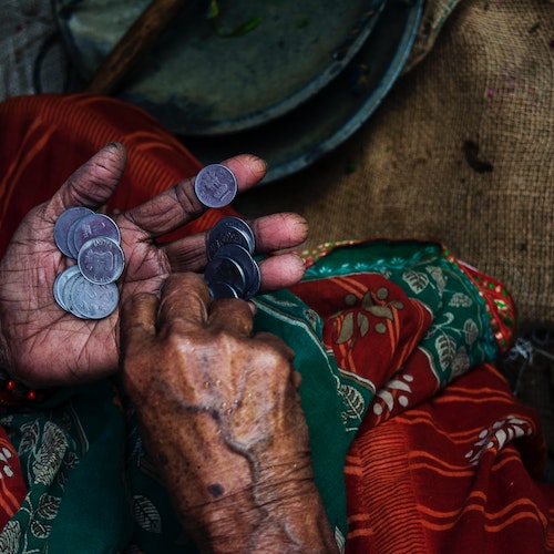 An old woman in traditional Indian clothes with a small number of coins in her palm