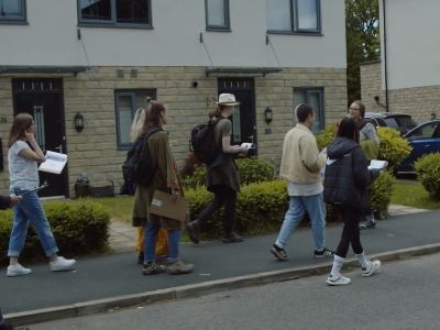 Several people with pamphlets walking along an urban street beside a building