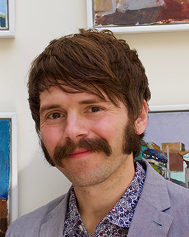 Chris, brown short hair, moustache smiling at the camera. 