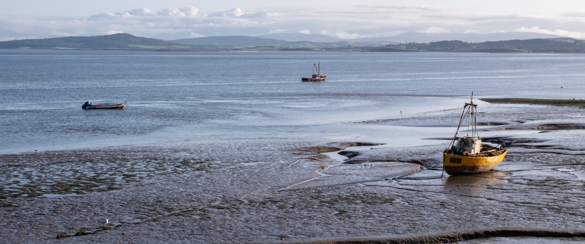 Boats rest on the mudflats of Morecambe Bay, while the Lake District hills loom in the background.