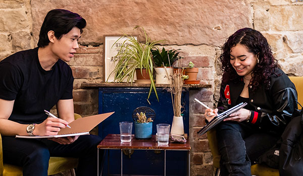 Two students sit and chat in a modern cafe.