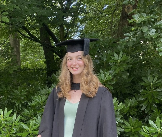 Dulcie in Graduation Attire in front of green foliage