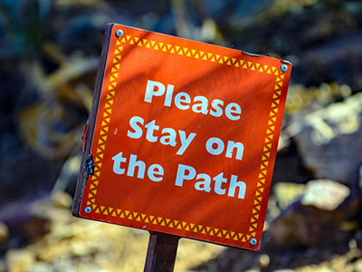 An orange sign saying please stay on the path.