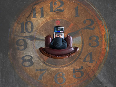 A hooded man sitting crossed legged with a laptop in the centre of a huge clock floor mosaic.