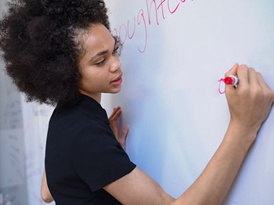 A woman writing on a whiteboard with red pen.