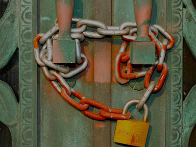 A rusted metal fence, locked by a thick chain and padlock.