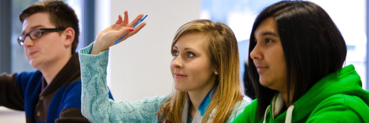 three students in seminar, one with hand raised