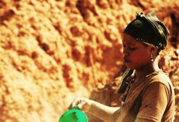 African female miner working in front of orange sandstone rockface