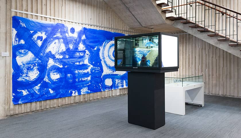 View of traces exhibition with large blue painting and magic box showing video of it being created.