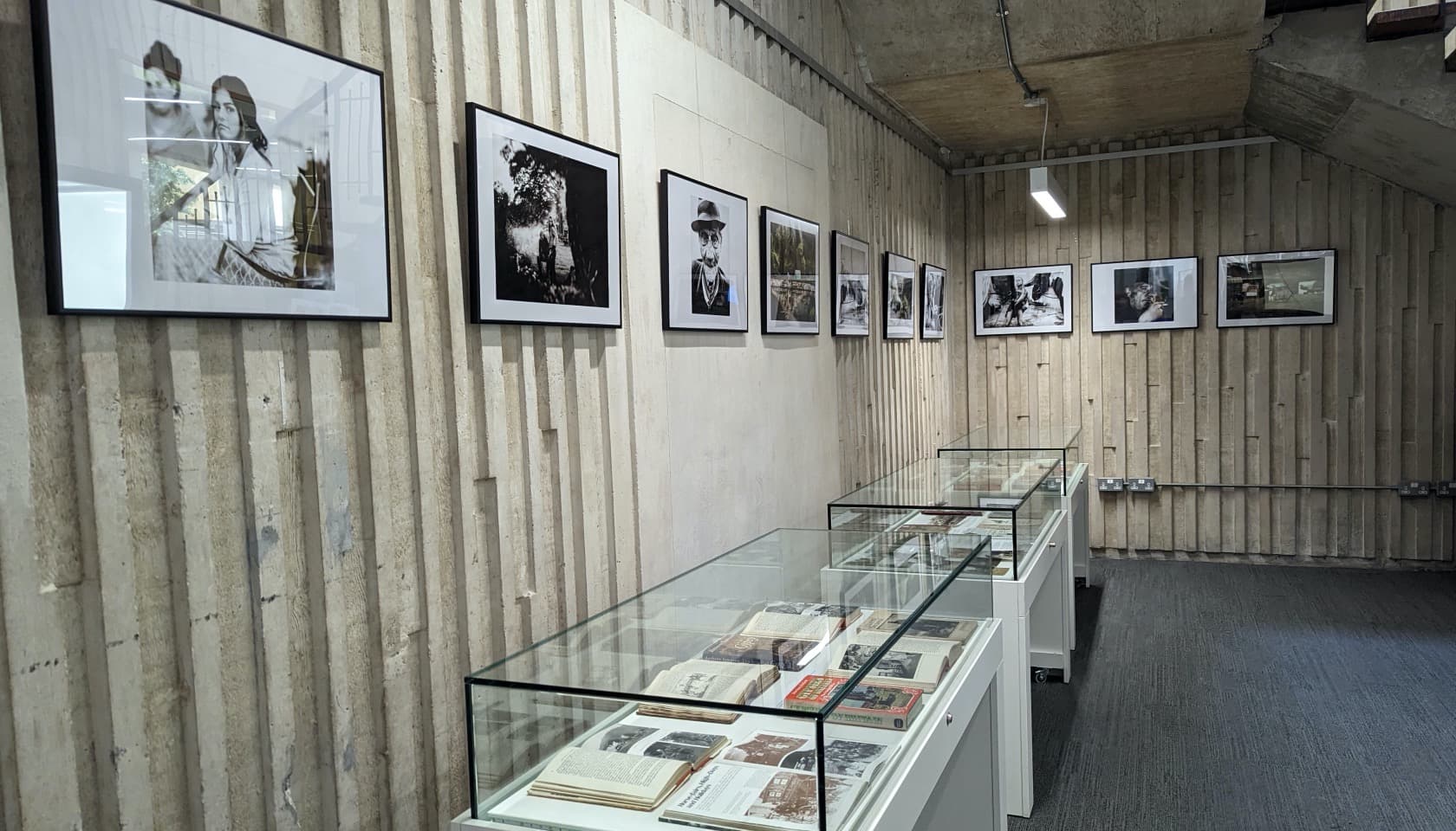 Three exhibition cases against a wall with framed photographs above them.