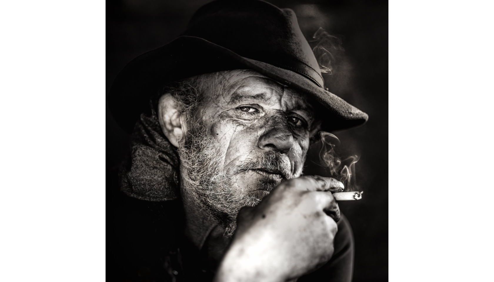 A man wearing a hat and holding a cigarette in his right hand.