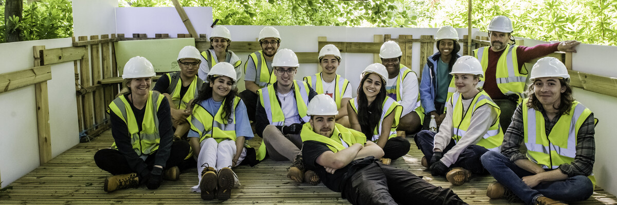 Architecture students lounge on a timber patio surrounded by trees.