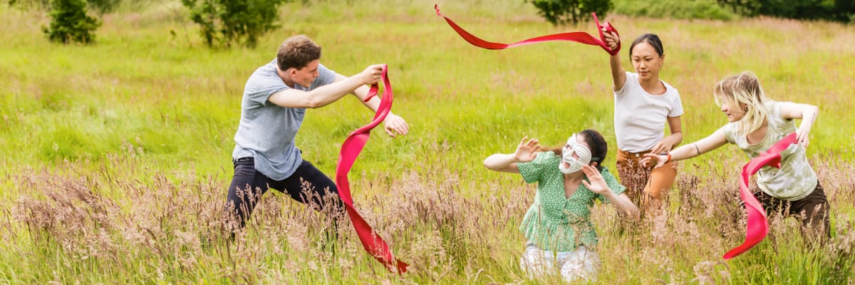 Theatre students perform in a field with ribbons and masks.