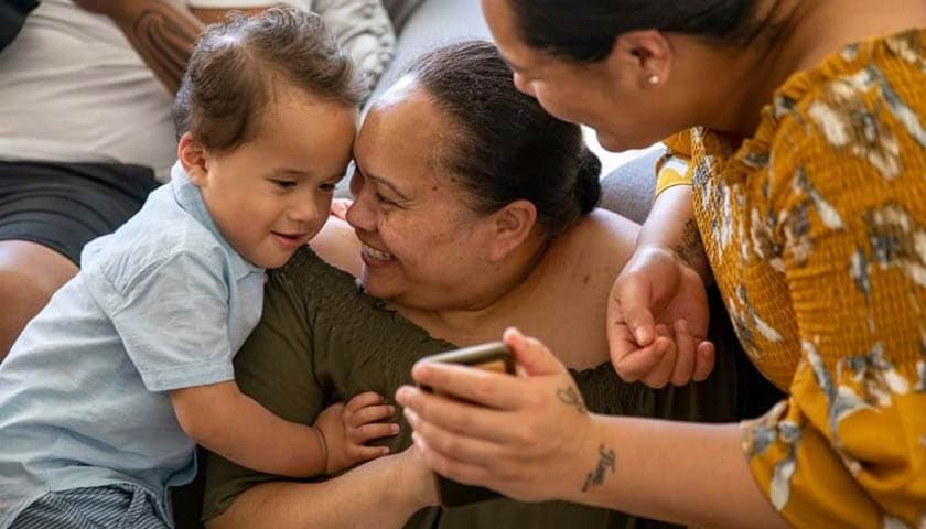 Woman holding a toddler who is avidly looking at a mobile phone held by another woman