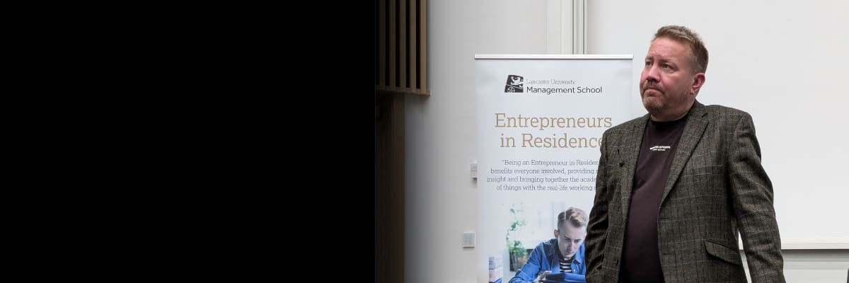 A man in a jacket leaning on a desk on stage.