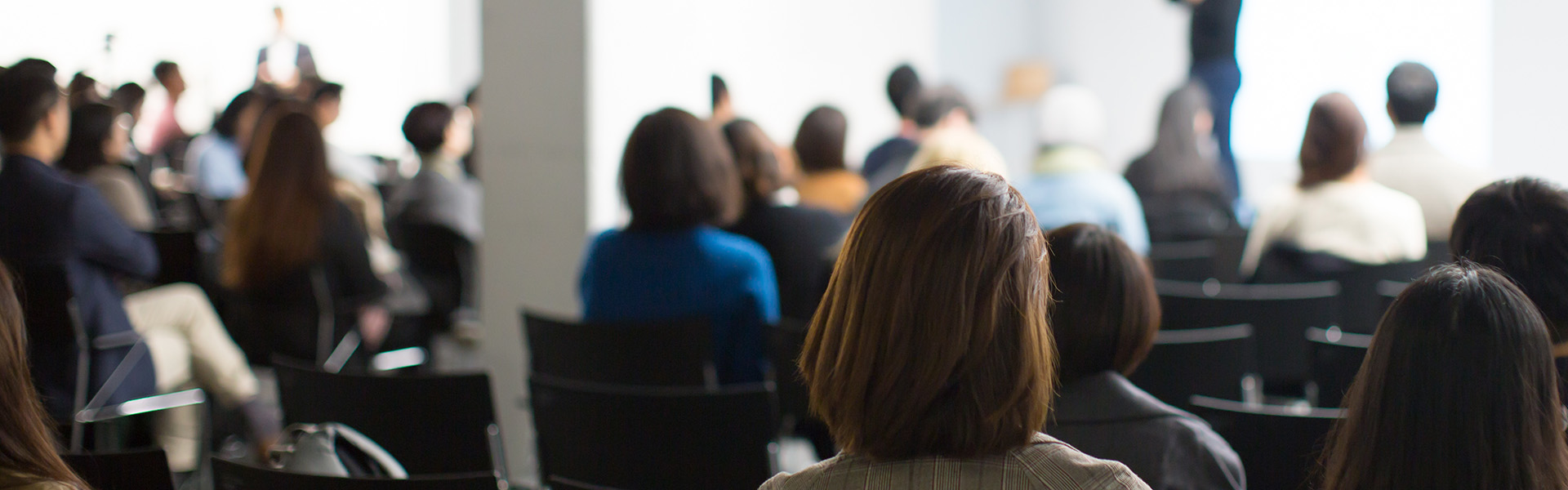Attendees in the audience of an event featuring a speaker on a stage