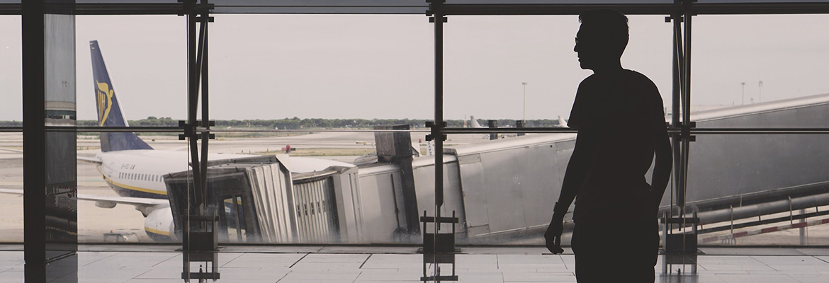 A person at an airport silhouetted in front of a window looking down onto a runway