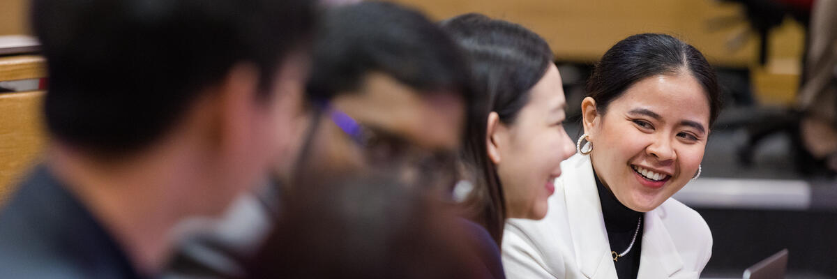 MBA students in the classroom, the focus is on a smiling female student wearing a white suit jacket 
