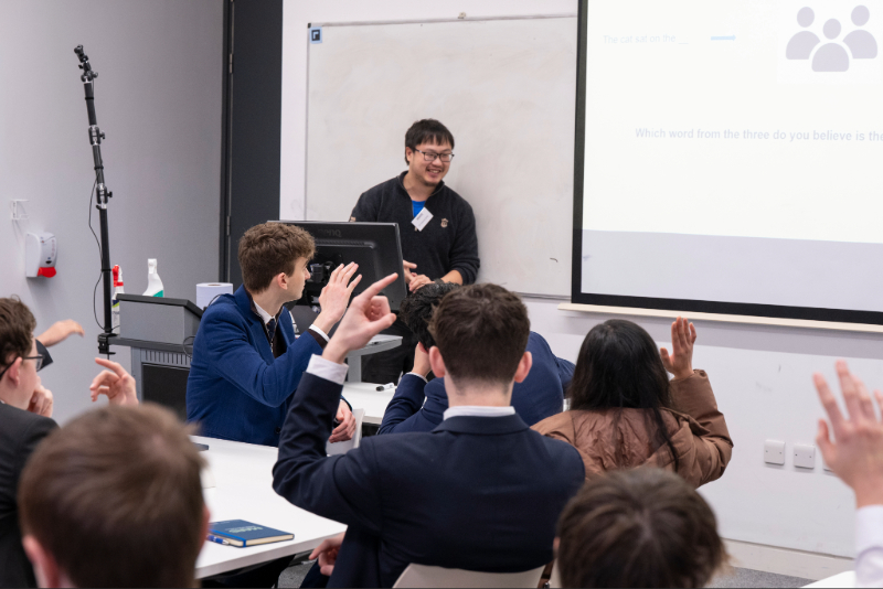 A lecturer asking a group of students to put their hands up and answer a question.