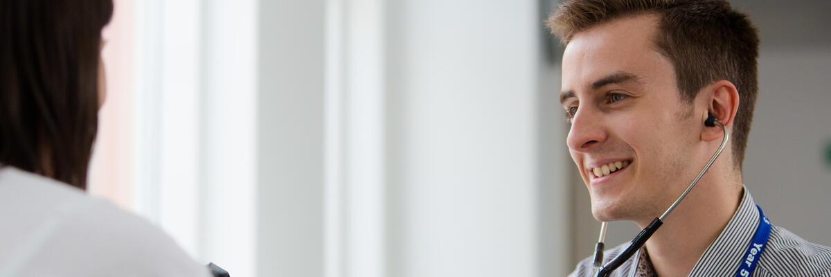 Student with stethoscope in ears treating a patient