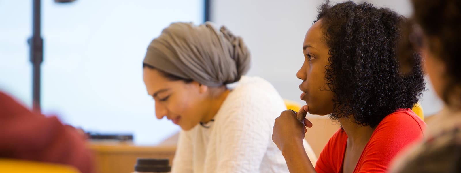 Image of two students - one looks down at her work and one focuses ahead