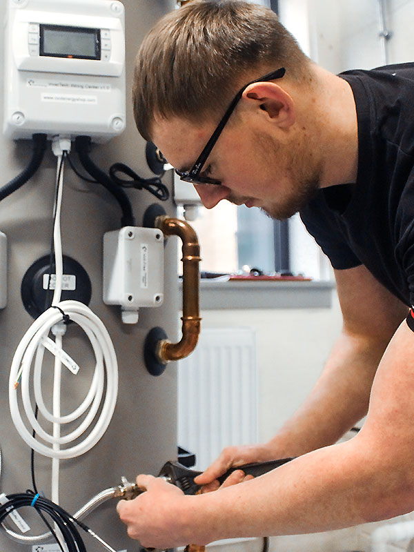 A young man uses a wrench on some pipework