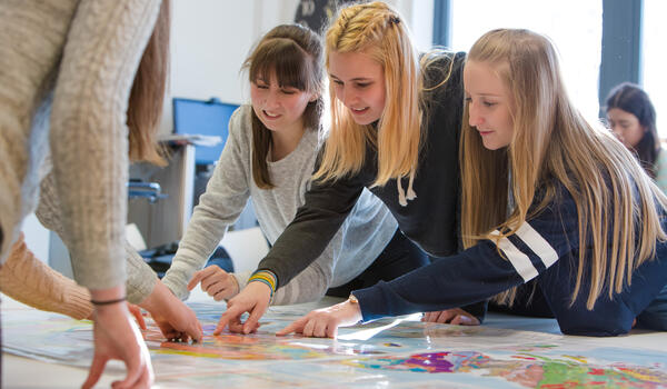 Students pointing at a colourful map to identify a natural disaster