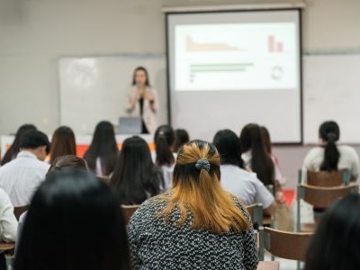 Rear view of college students listening to a teacher teaching and explaining lesson in classroom