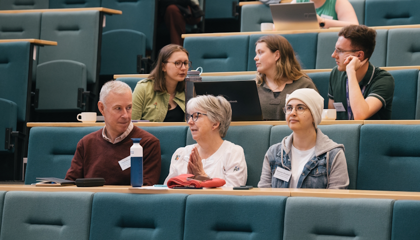 6 people sitting in a lecture theatre talking, waiting for an event to begin.