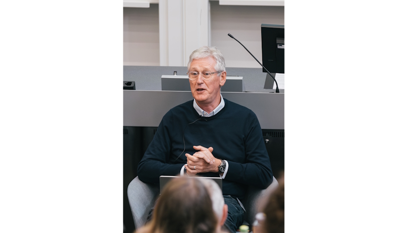 Duncan Pollard seated in chair, in the middle of speaking to an audience.
