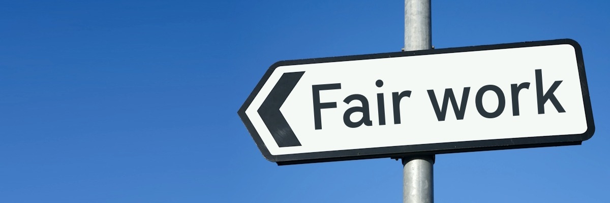 A white road sign pointing to the left with the words 'Fair work' written on it.