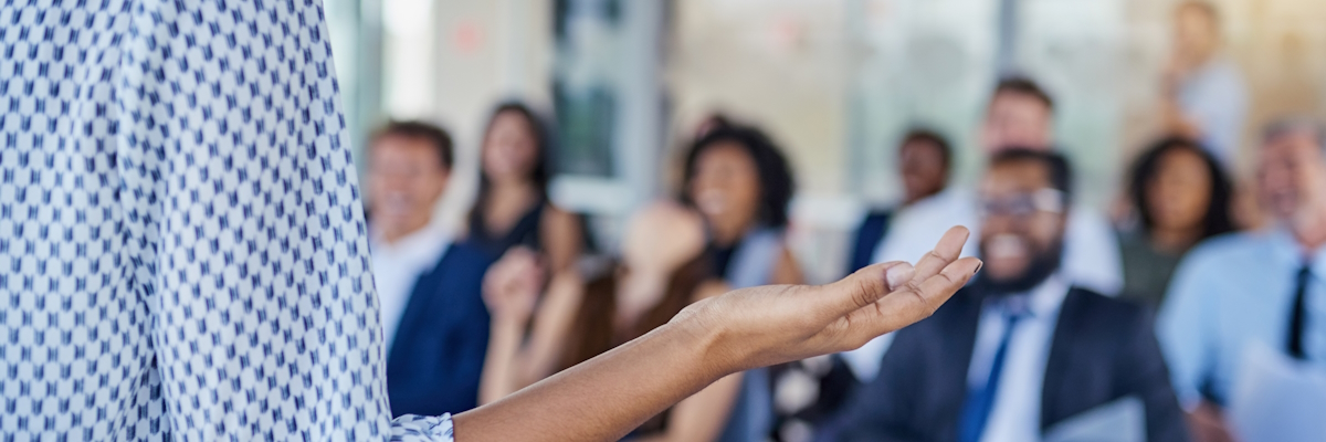 A person gesticulating with their right hand in front of an audience of businesspeople.