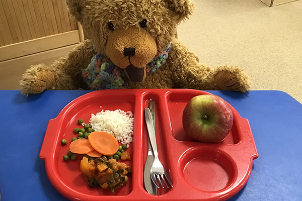 Eden Bear sits at the table with a plate of food from the Pre-School