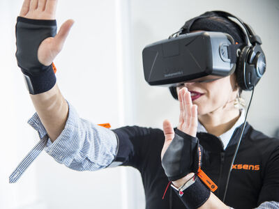 A student immersed in virtual reality wearing goggles and raising their hands