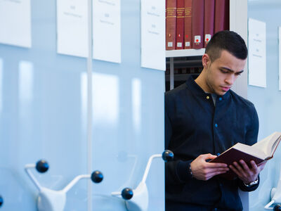 Student reading book next to library bookshelves