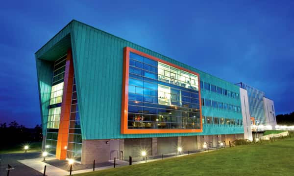 InfoLab21 in the evening, with the green and orange building lit up.