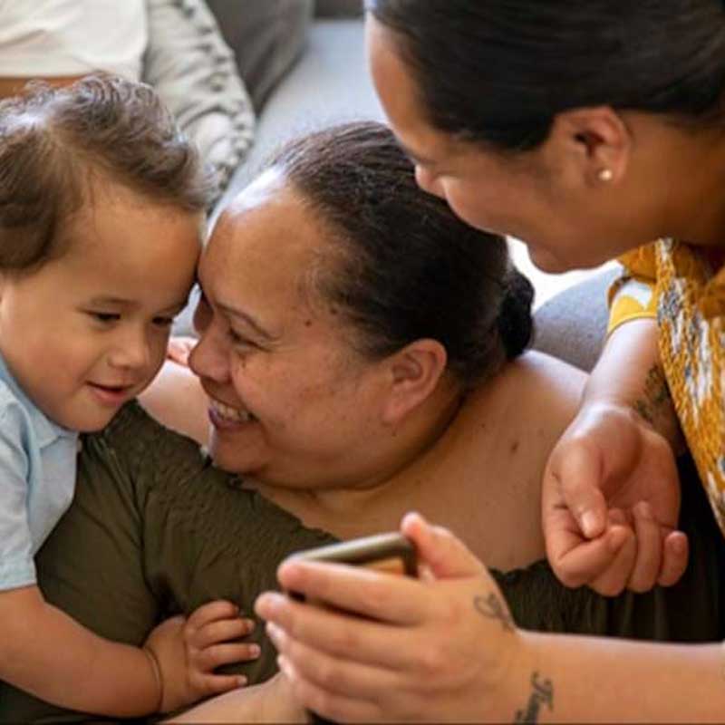 A stock image of 3 people including a young boy engaging with a smartphone while talking and laughin
