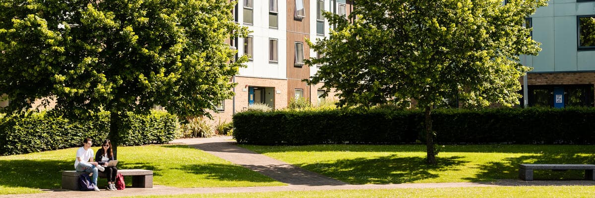 Two people sat on a bench in the sunshine outside county college