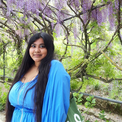 Ruwaida, wearing a blue dress standing under a purple flowering tree
