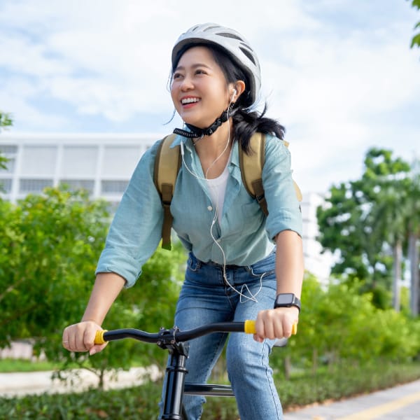 A person smiles as they ride a bike past green foliage.