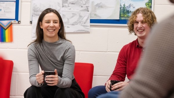 Photo of smiling STOR-i students in a communal social space, surrounded by art created in the STOR-i support group, and DiverSTOR-i progress pride flag.