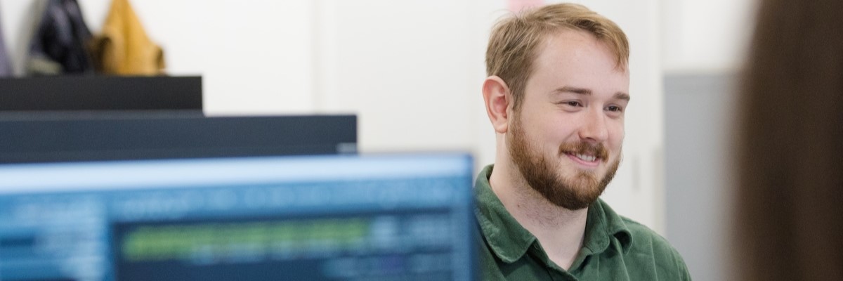 Student smiling behind a computer monitor